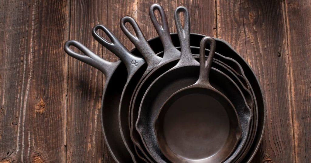Several sizes of cast iron skillets stacked against a wooden background | Benefits of a Cast Iron Skillet