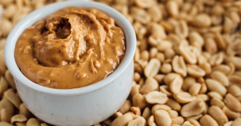 Peanut Butter in a ceramic ramekin set on top of a bunch of raw peanuts