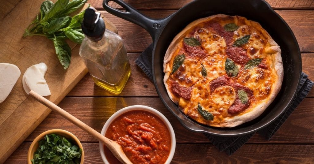 Gluten-free pizza in a cast iron skillet with pizza ingredients spread out around the pan
