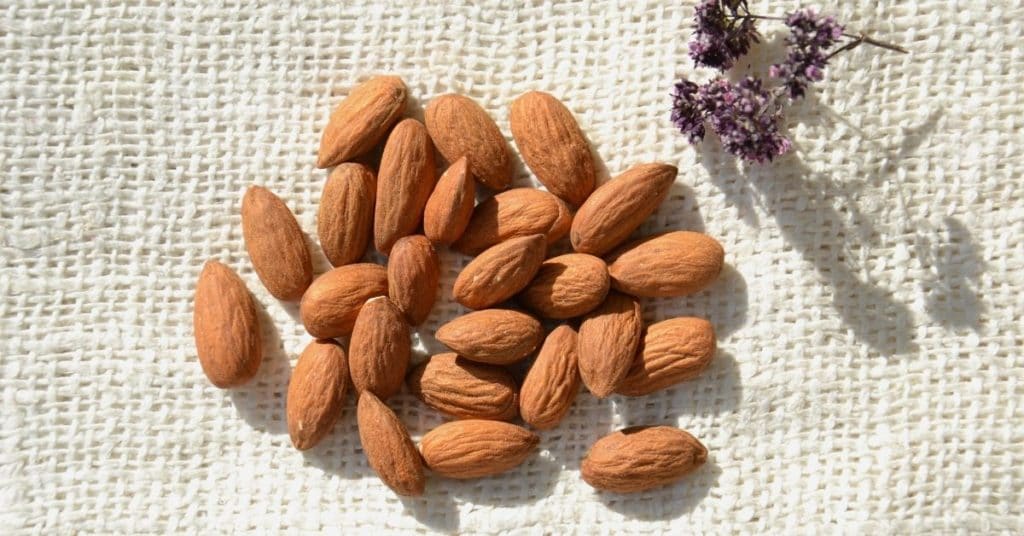 A handful of almonds, a great source of calcium, lie on a woven cloth with some dried flowers next to them