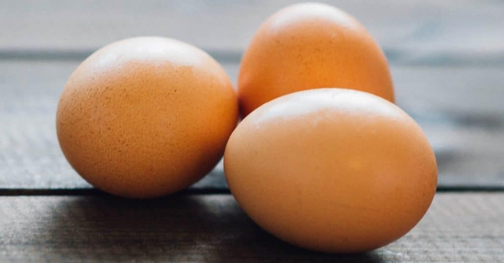 Three brown eggs, a great food source of zinc for those with gluten intolerance, are nestled together on a wooden background