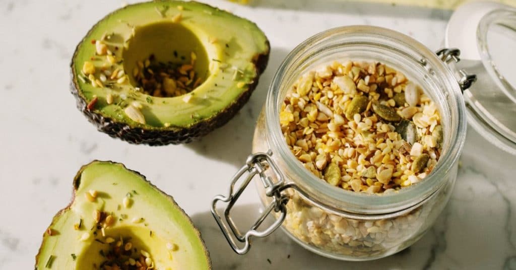An avocado sliced in half topped with a mixture of nuts and seeds