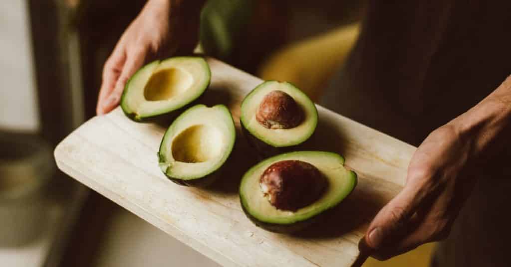 Avocado Benefits for Health, A persons hands hold out a cutting board with two ripe halved avocados
