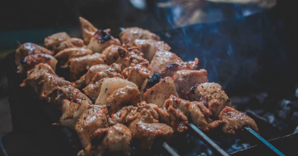 Chicken in small pieces on kebab sticks set over an outdoor grill