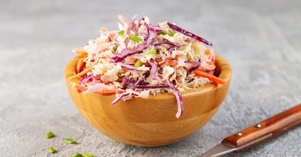 Outdoor Easy Summer Dinner Party Menu, A large mound of coleslaw is set in a wooden bowl on a blurred out background
