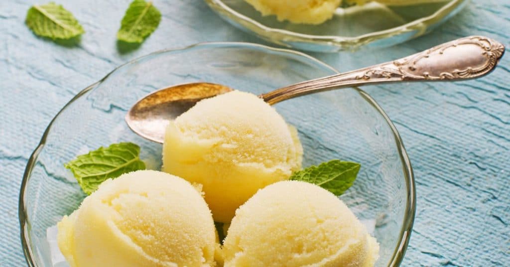 Three scoops of sorbet are set out in a clear dish garnished with mint leaves