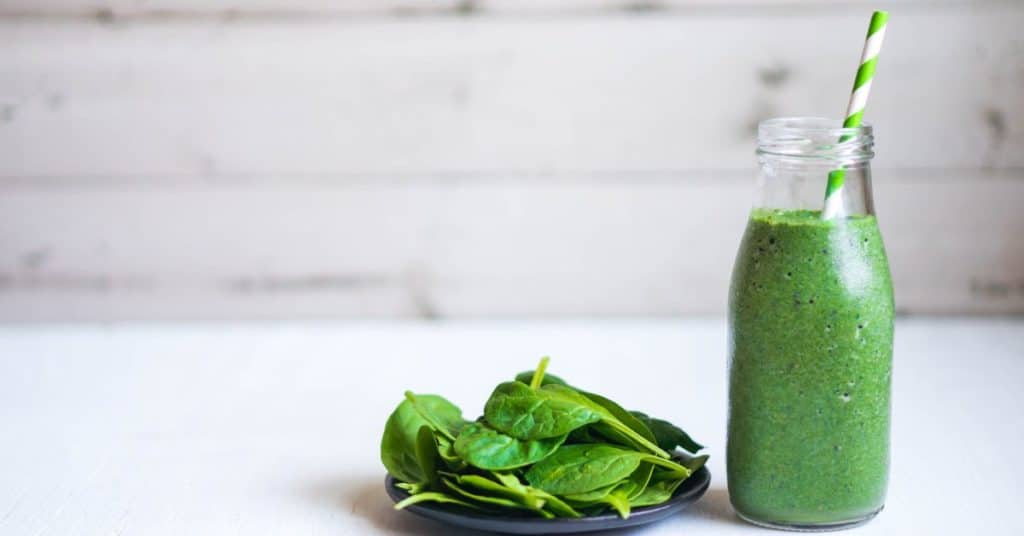 A green smoothie, with a handful of greens set out next to the glass