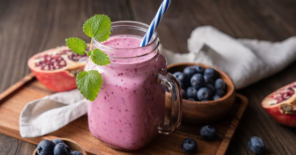 A smoothie topped with mint and pomegranate and blueberries in the background