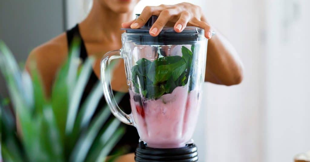 A woman places the top on her blender to blend up greens and fruit, How to Make a Healthy Smoothie