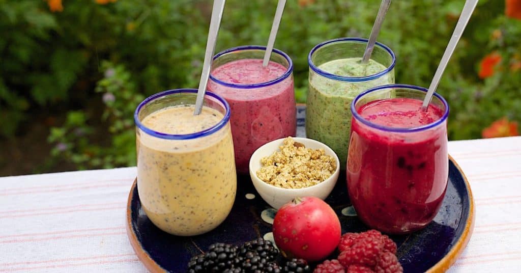 Four different smoothies presented on a plate with fresh fruit and granola, How to Make a Healthy Smoothie