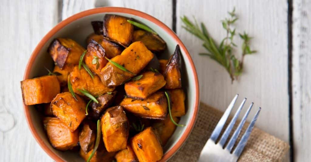 A cubed sweet potato roasted and topped with fresh rosemary in a bowl