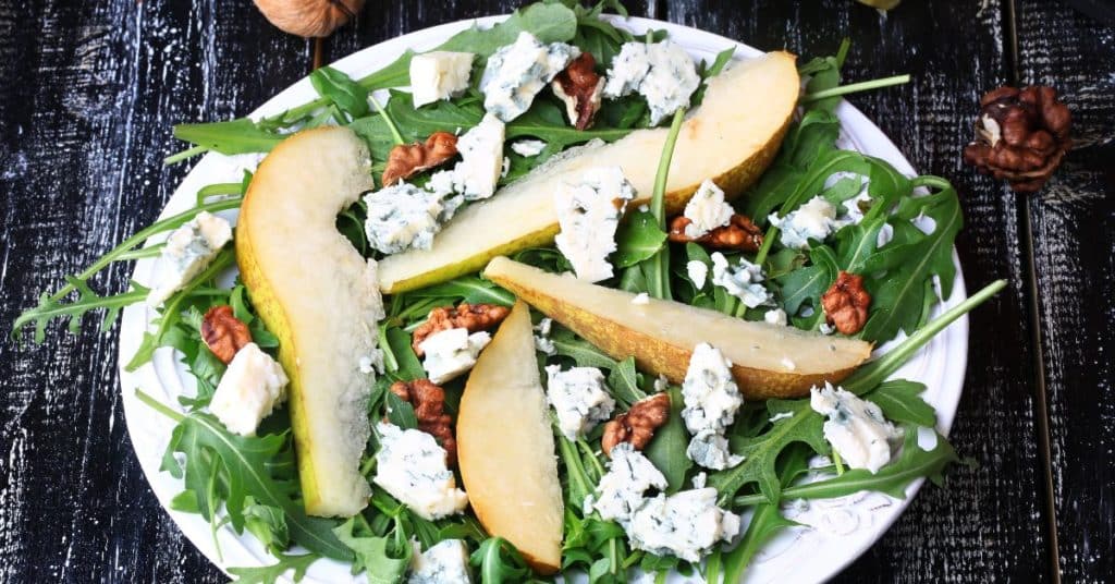 A pear sliced on top of a bed of arugula, garnished with blue cheese and walnuts