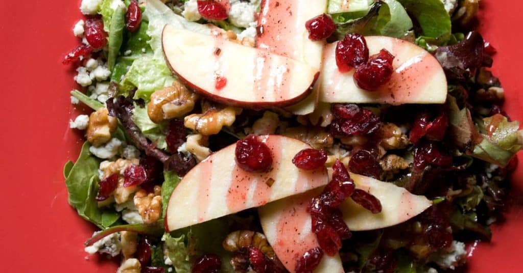 Multiple, quercetin-rich seasonal fall foods, like apples and cranberries top a salad along with goat cheese and walnuts