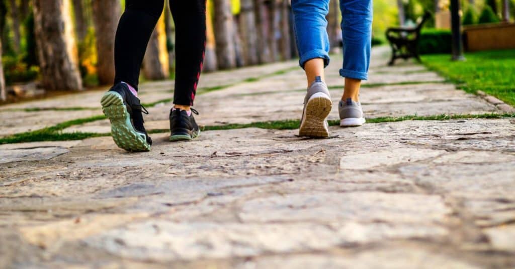 Two woman's feet and legs in sneakers walking down a stone pathway