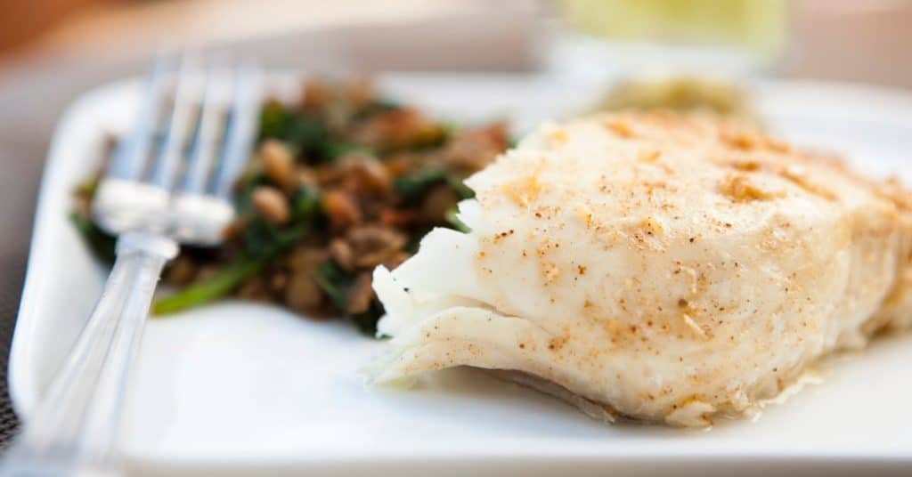 A thick fillet of seasoned white fish sits on a plate
