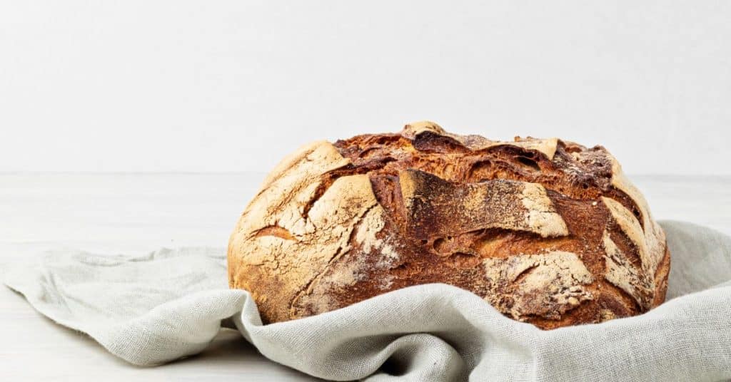 A fresh floured loaf of sourdough bread sits on a kitchen towel, Benefits of Gluten Free Sourdough Bread