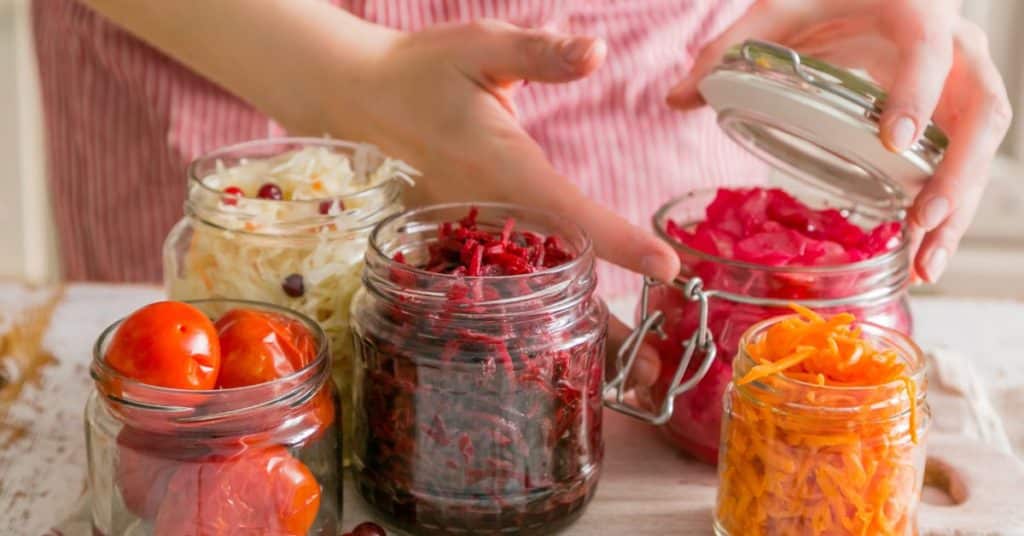 A woman's hands close up a sealed jar of fermented foods, while several other jars with different fermented products wait to also be capped