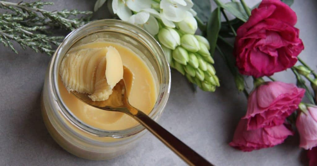 A spoon lifts out a smooth hunk of ghee from a jar