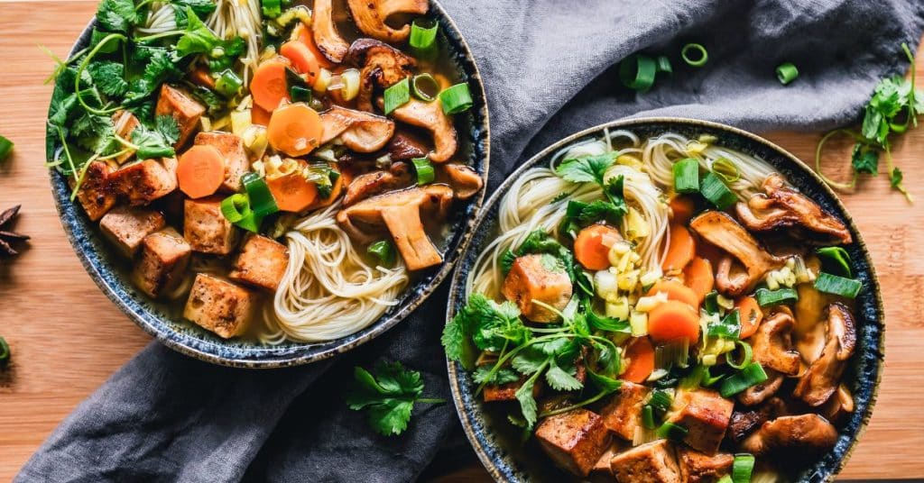 A colorful ramen bowl with herbs, green onion, carrots, and mushrooms