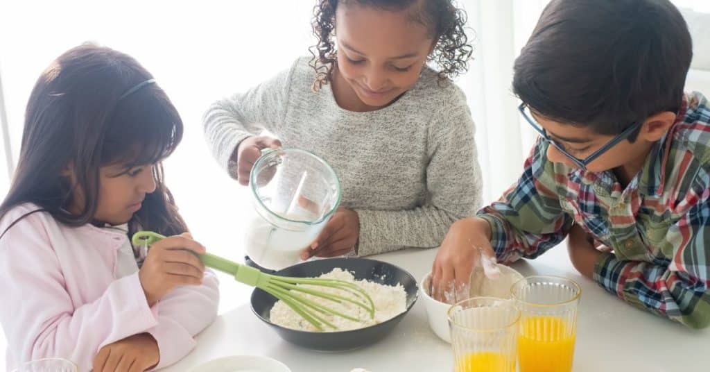 Three children make pancake batter together acting as if it's a science experiment