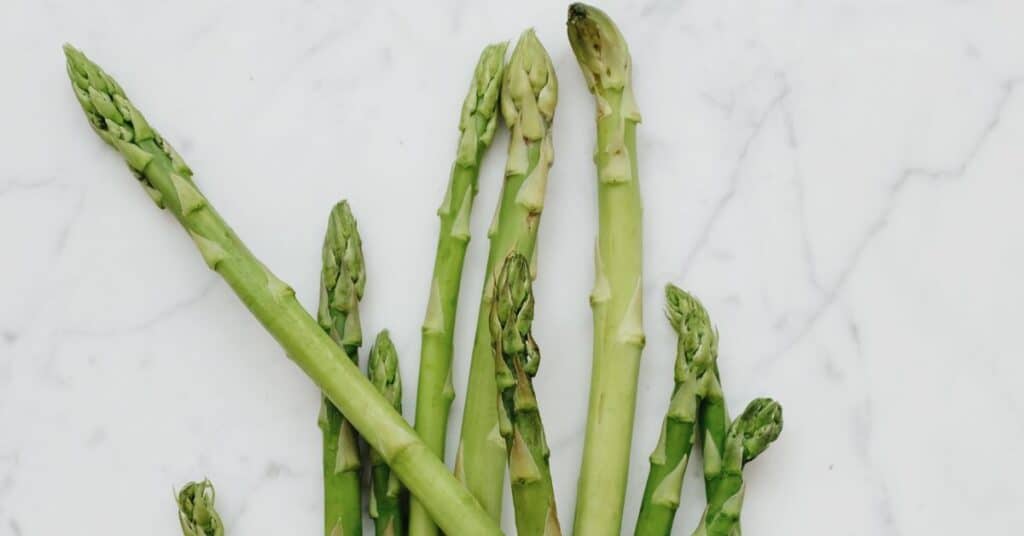 Tips of a bunch of asparagus are strewn on a marble countertop, foods to help detox