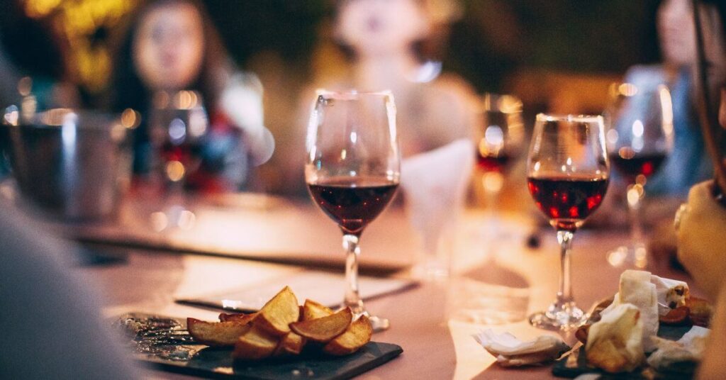 A blurred scene at a restaurant focused on two glasses of wine and potato wedges