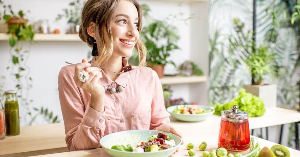 A woman eats a beet and veggie salad with a smile on her face