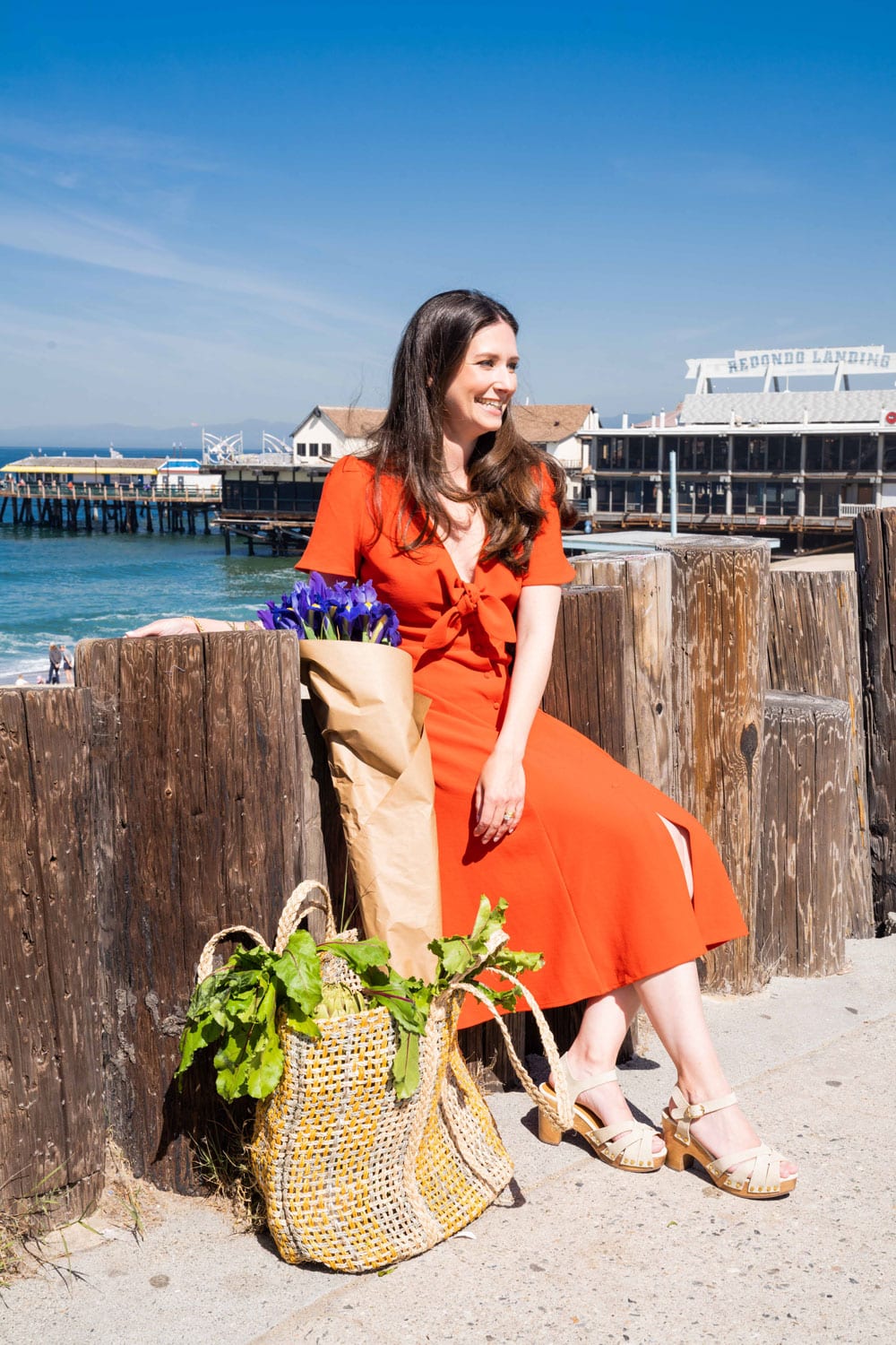 Emily Luxford, autoimmune, pediatric and food sensitivity dietitian, stands with goodies from the farmers market on a California pier