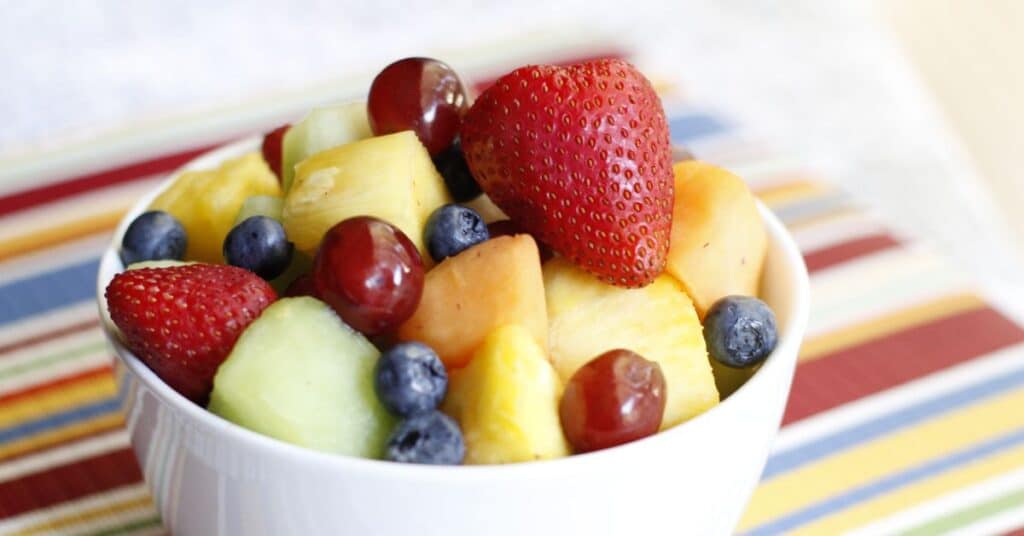 A bowl of fresh fruit, including grapes, strawberries, blueberries, along with diced cantaloupe, honeydew and pineapple