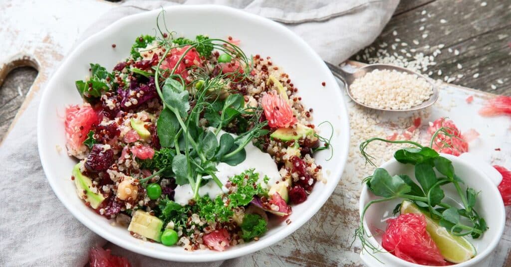 A bowl of quinoa topped with herbs, kale, avocado and grapefruit