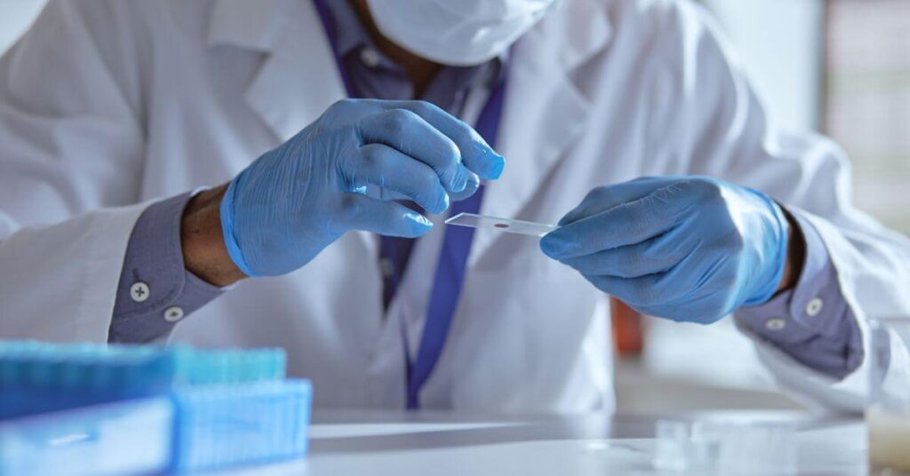 A man in a lab coat and rubber gloves looks at a blood sample, celiac testing