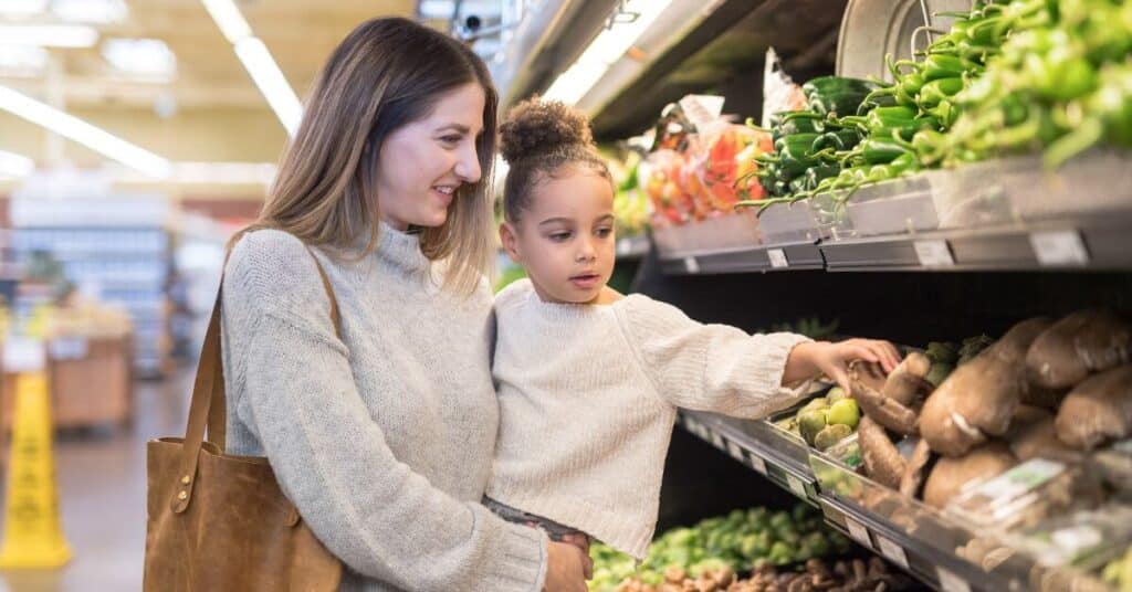 A mother carries her daughter as they shop in the produce section of a grocery store
