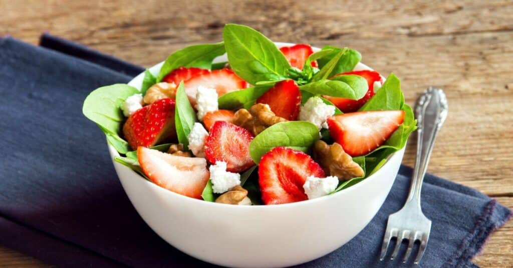Naturally gluten free salad in a bowl with spinach, walnuts, feta, and strawberries