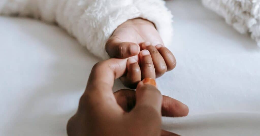 A mom places one of her fingers in the grasp of a tiny baby's hand