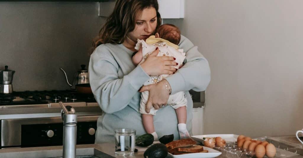 A new postpartum mom holds her new baby in the kitchen as she decides what to eat after giving birth and breastfeeding