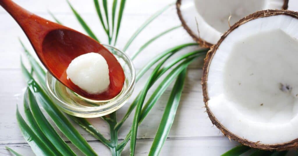 A dollop of coconut oil in a wooden spoon set next to a halved coconut