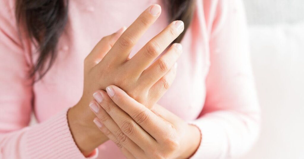 A woman holds her hand as if it's in pain from inflamed joints, Anti-inflammatory Diet Vs Autoimmune Diet inflammation