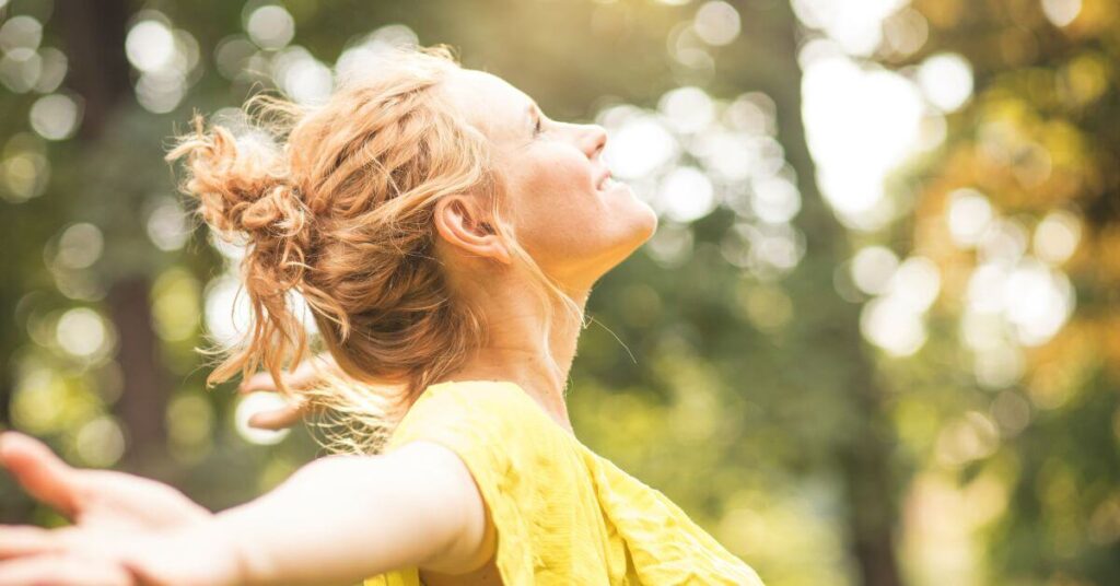 A woman standing outside smiles and looks up towards the sun