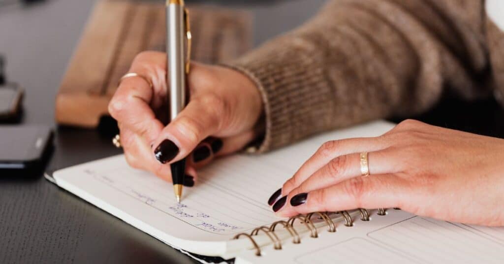 Woman with painted black nails holding a pen writing in an open food journal