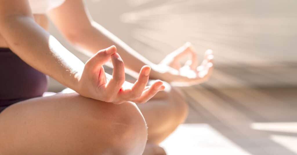 Close up of a woman doing yoga sitting with her hands resting on her knees in the sun, intermittent fasting