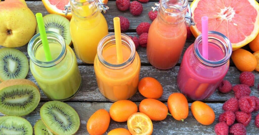 Freshly squeezed green, orange and pink juice surrounded by kiwis, raspberries oranges and grapefruit