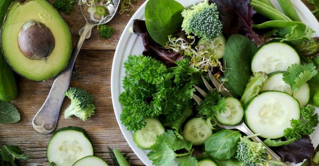 A fiber-rich salad with leafy greens, broccoli, cucumber and avocado in a bowl on a wooden table, How to Lower Insulin Quickly