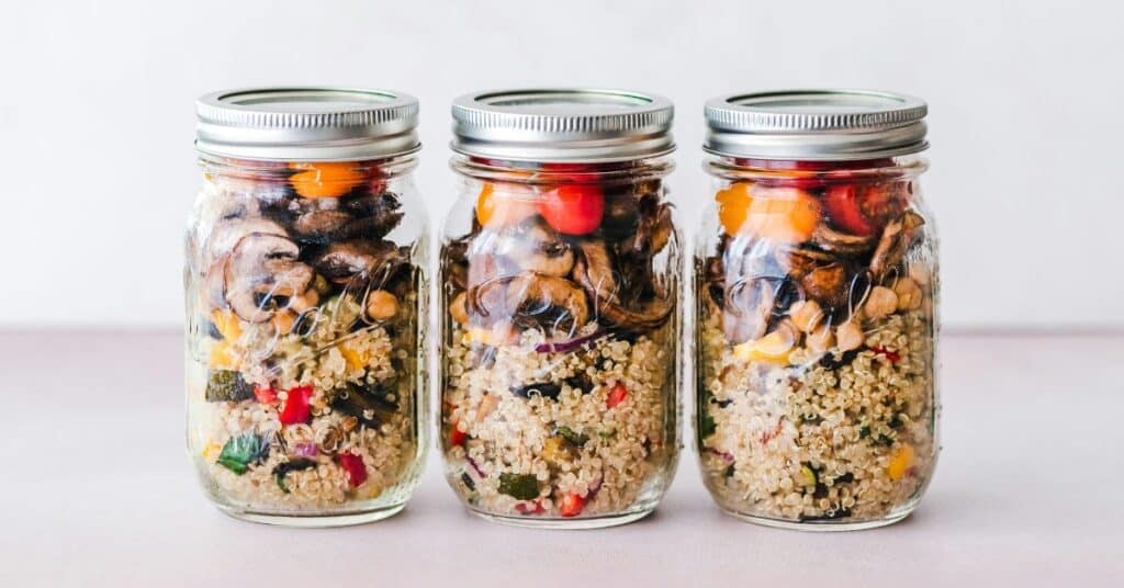 Three glass meal prep jars with quinoa, mushrooms, chickpeas and vegetables