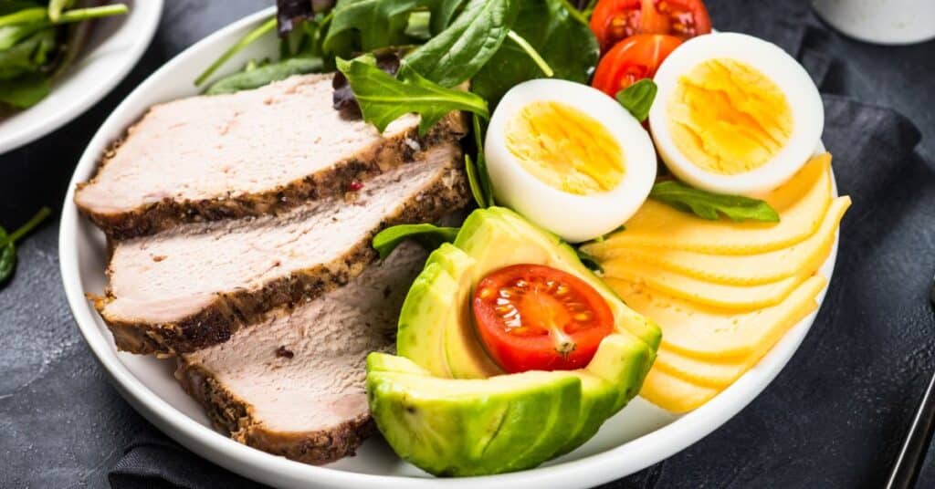 Plate with pork chops, avocado, cheese, boiled egg, tomato and lettuce, keto diet advantages and disadvantages