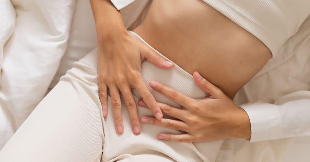 Woman laying on bed while holding cramping stomach