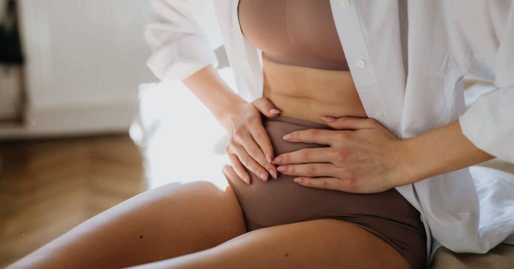 A sitting woman holding her stomach in discomfort, Signs Your Gut is Healing