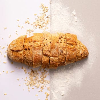 A loaf of bread shown sliced in half with one half oats and the other half flour, got glutened
