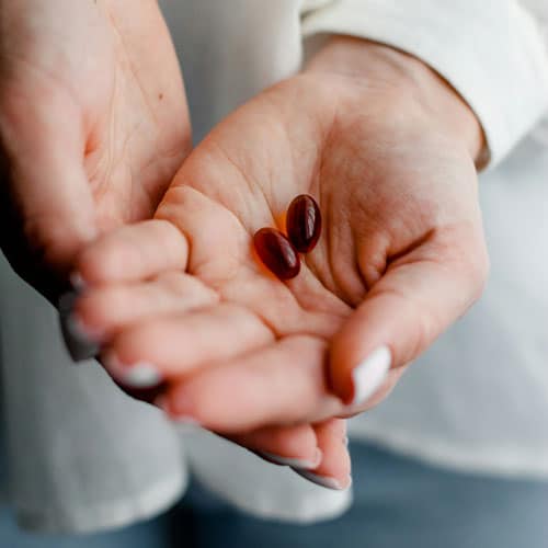 women holds cupped hand out with two gel supplements in it