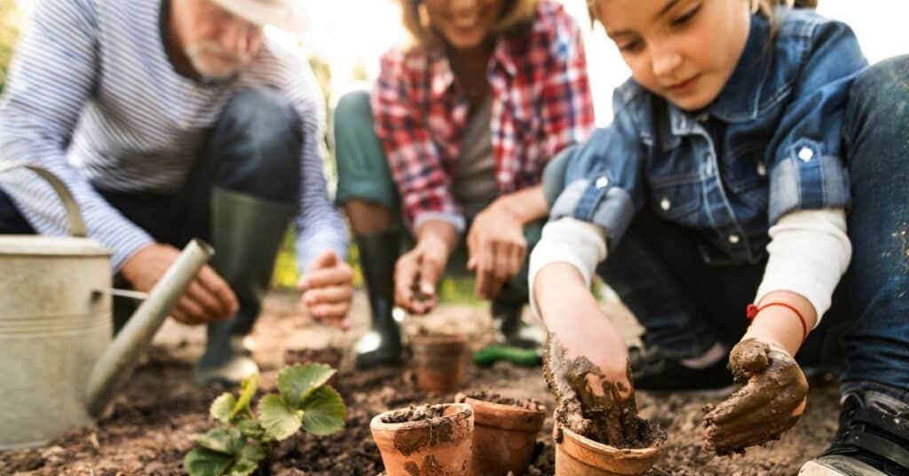 a mother, father and young child planting seeds in flower pots, gardening with kids