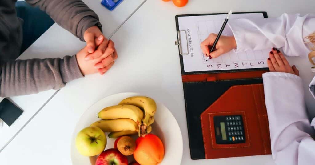 A man sitting at a table with a dietitian who is writing a meal plan next to a bowl of fruit, what does a registered dietitian do